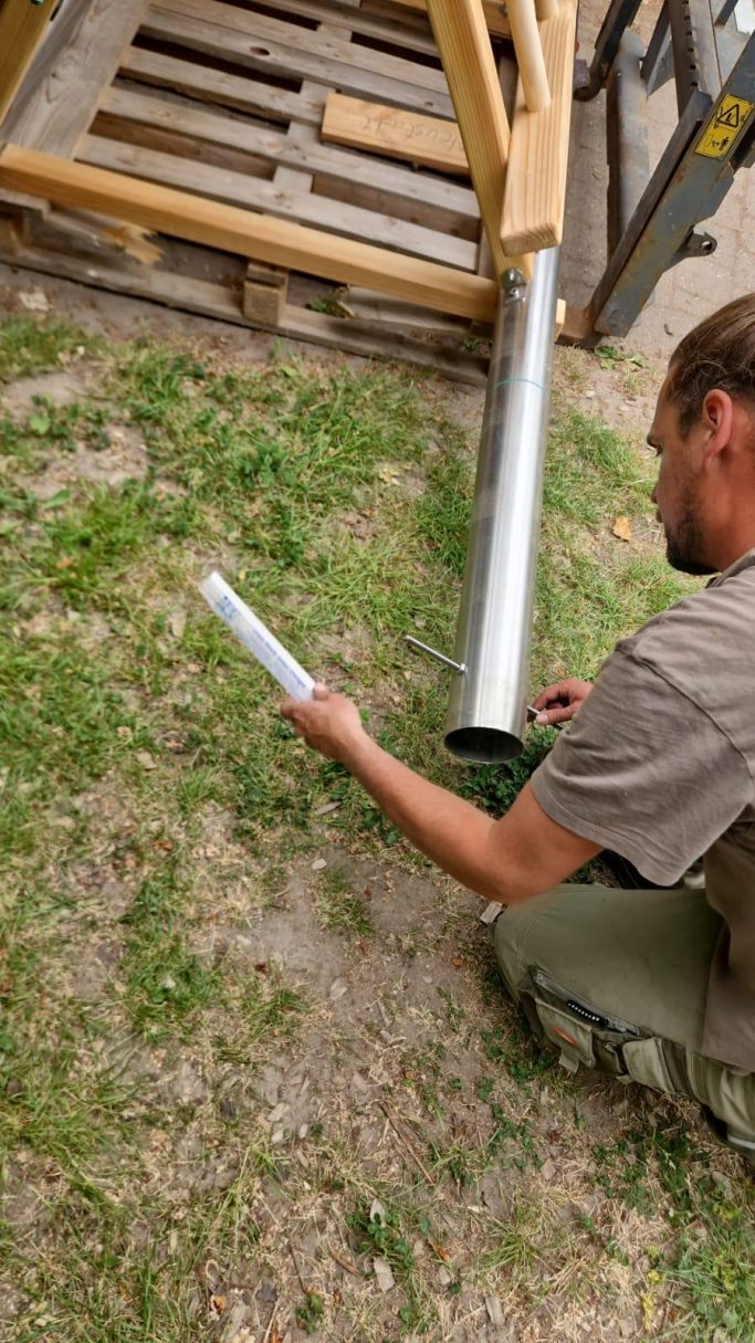 Mann misst mit einem Rohr in der Nähe einer Holzstruktur auf dem Boden.