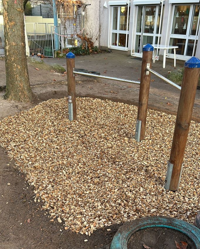 Spielplatzbereich mit einem Kiesbett und Holzpfosten.